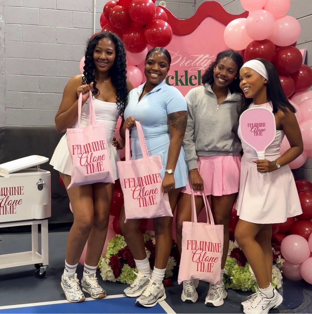 Attendees with Feminine Alone Time tote bags and paddle at the Pretty & Pickleball balloon arch