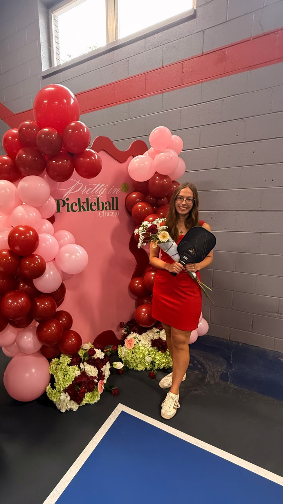 Attendee in a red dress holding a paddle and bouquet at the Pretty in Pickleball Chicago balloon arch