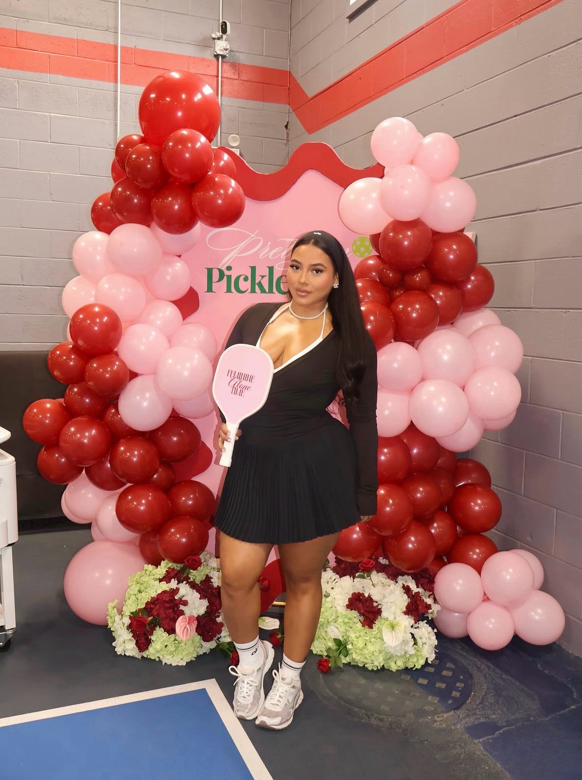 Attendee posing with paddle at the Pretty & Pickleball balloon arch